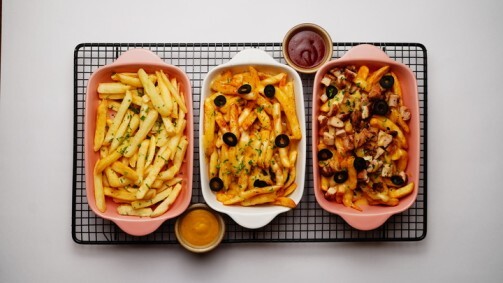 Three servings of German loaded fries with dipping sauce on a rack
